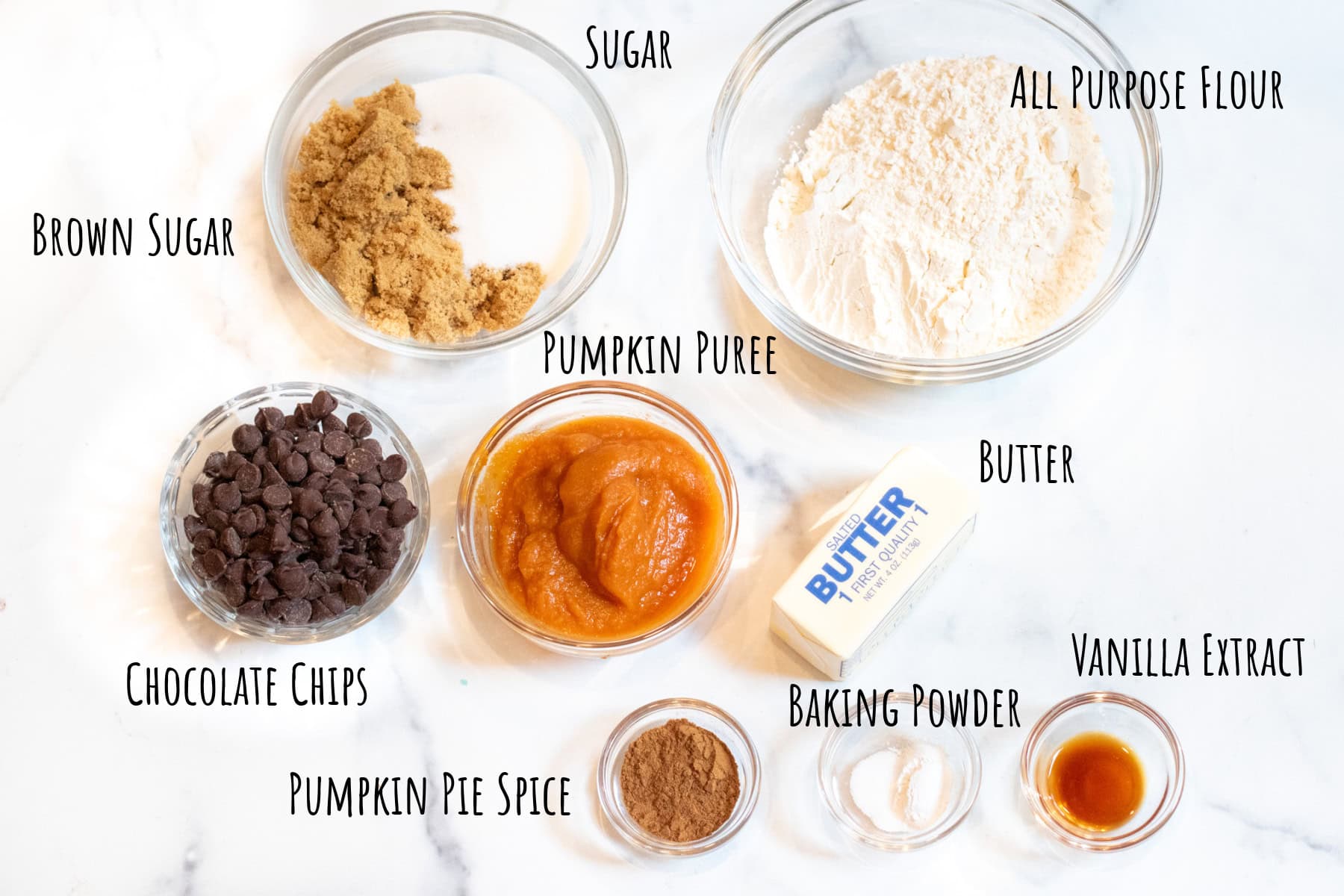 a bowl of sugars, flour, chocolate chips, pumpkin puree, butter, spices, and vanilla extract all labeled.