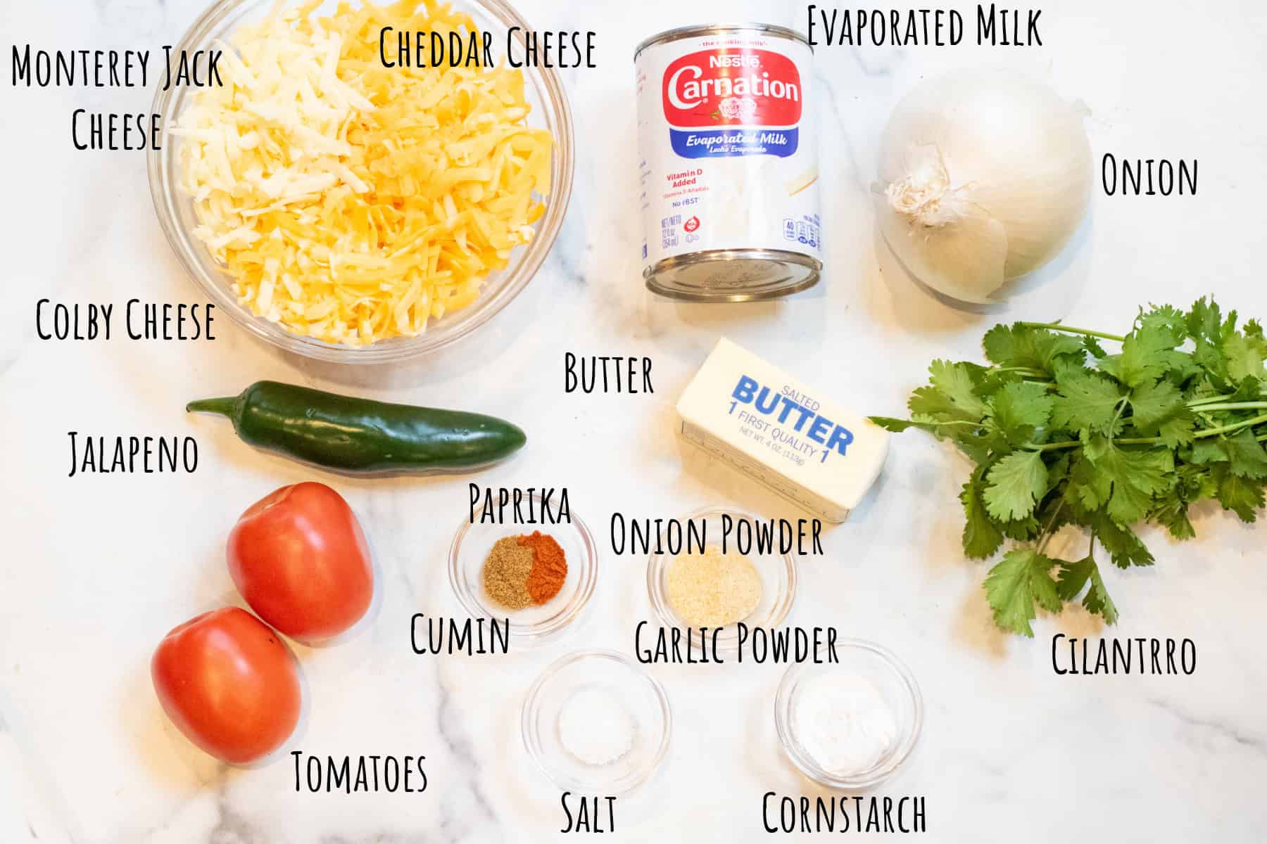 a bowl of shredded cheeses, can of evaporated milk, onion, jalapeno, tomatoes, spices, buter, and cilantro labeled.