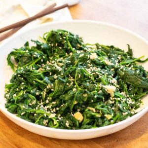 a bowl of blanched spinach with garlic and sesame seeds and chopsticks.