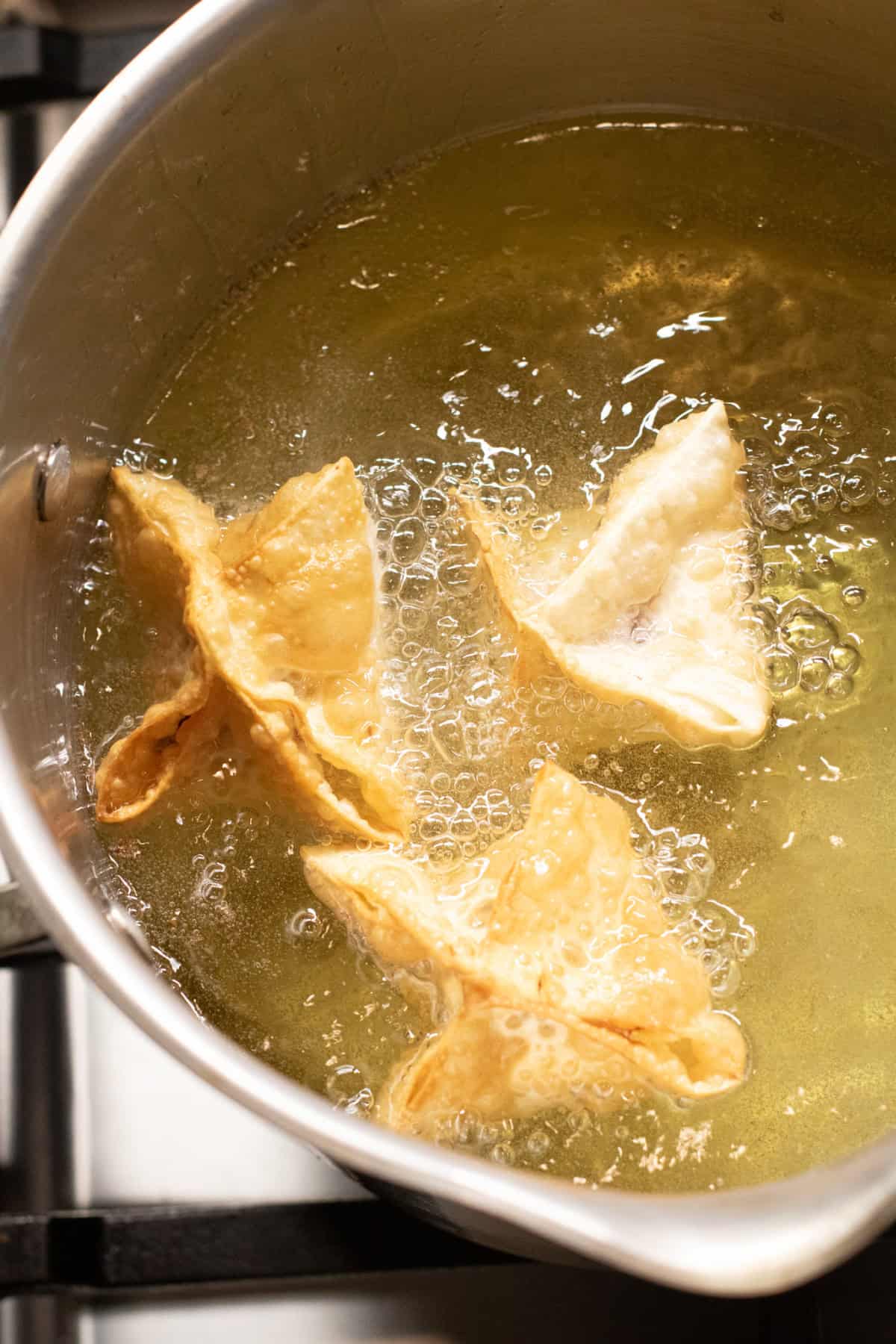 3 wontons frying in a pot of oil.