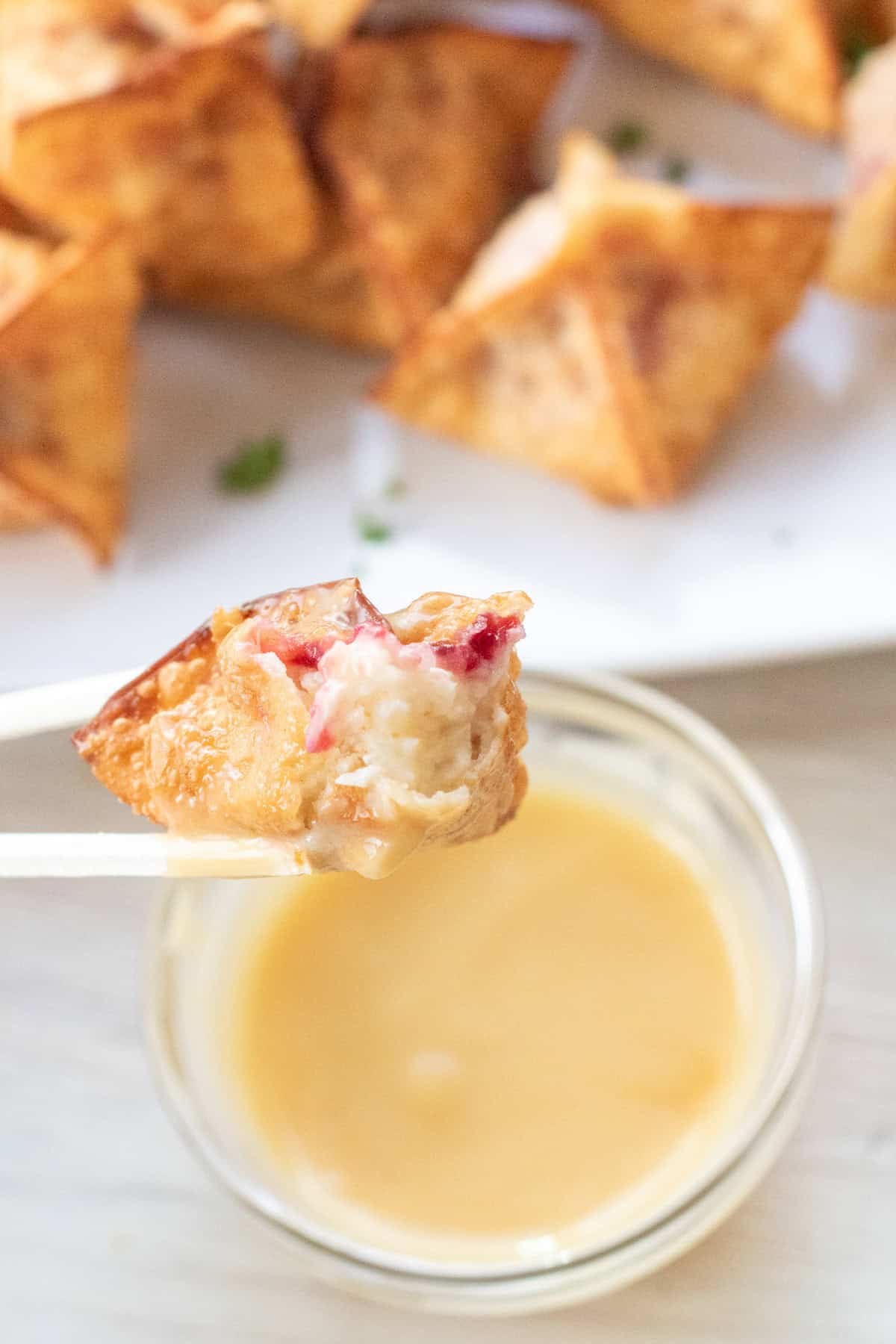 chopsticks holding up a wonton with half of it bitten off showing a mashed potato cranberry filling.