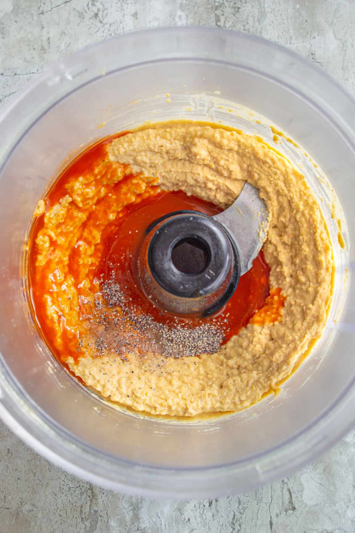 add buffalo sauce to the blended ingredients for buffalo hummus in a food processor.
