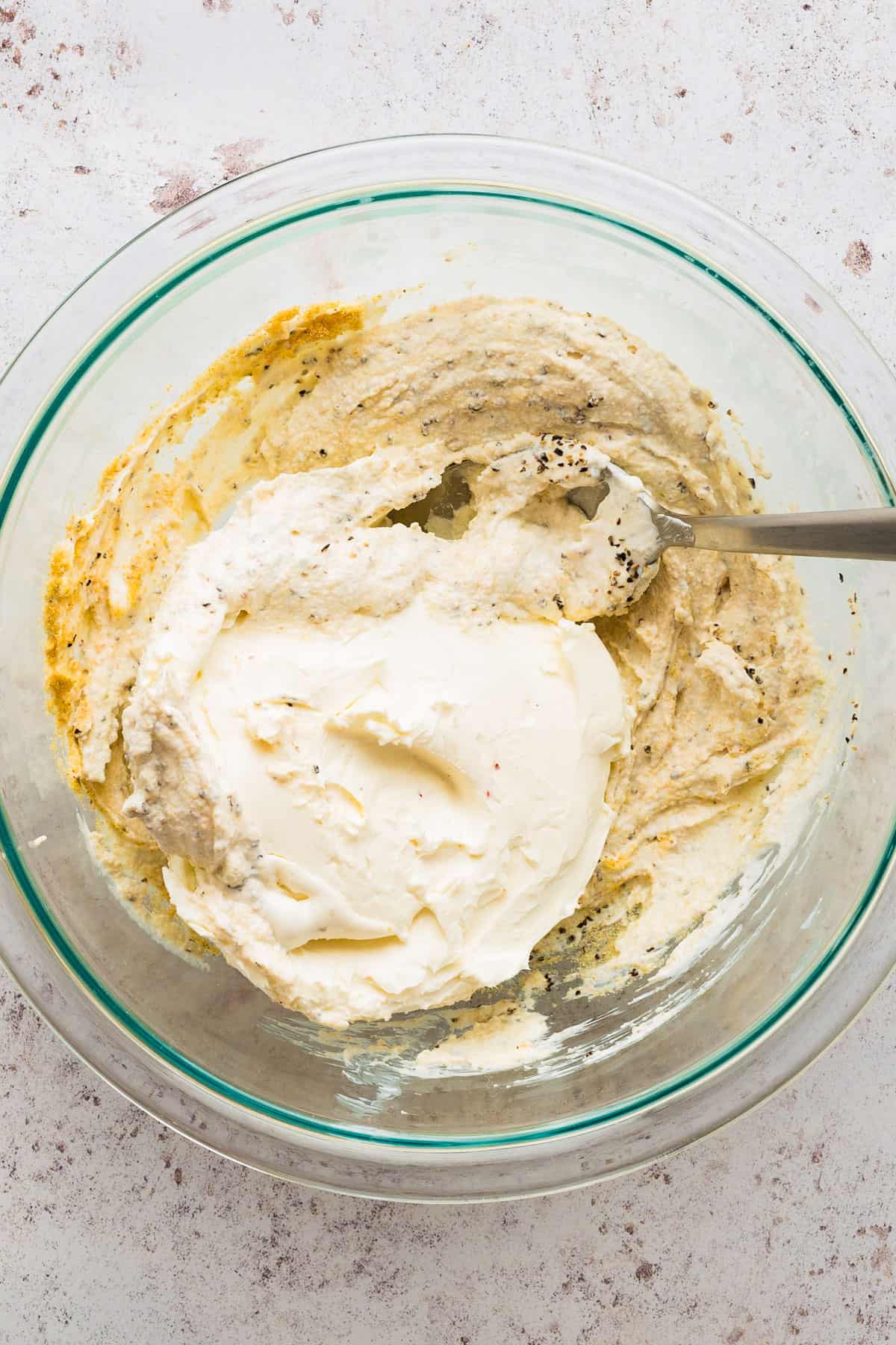 adding softened cream cheese to jalapeno popper dip in a bowl.