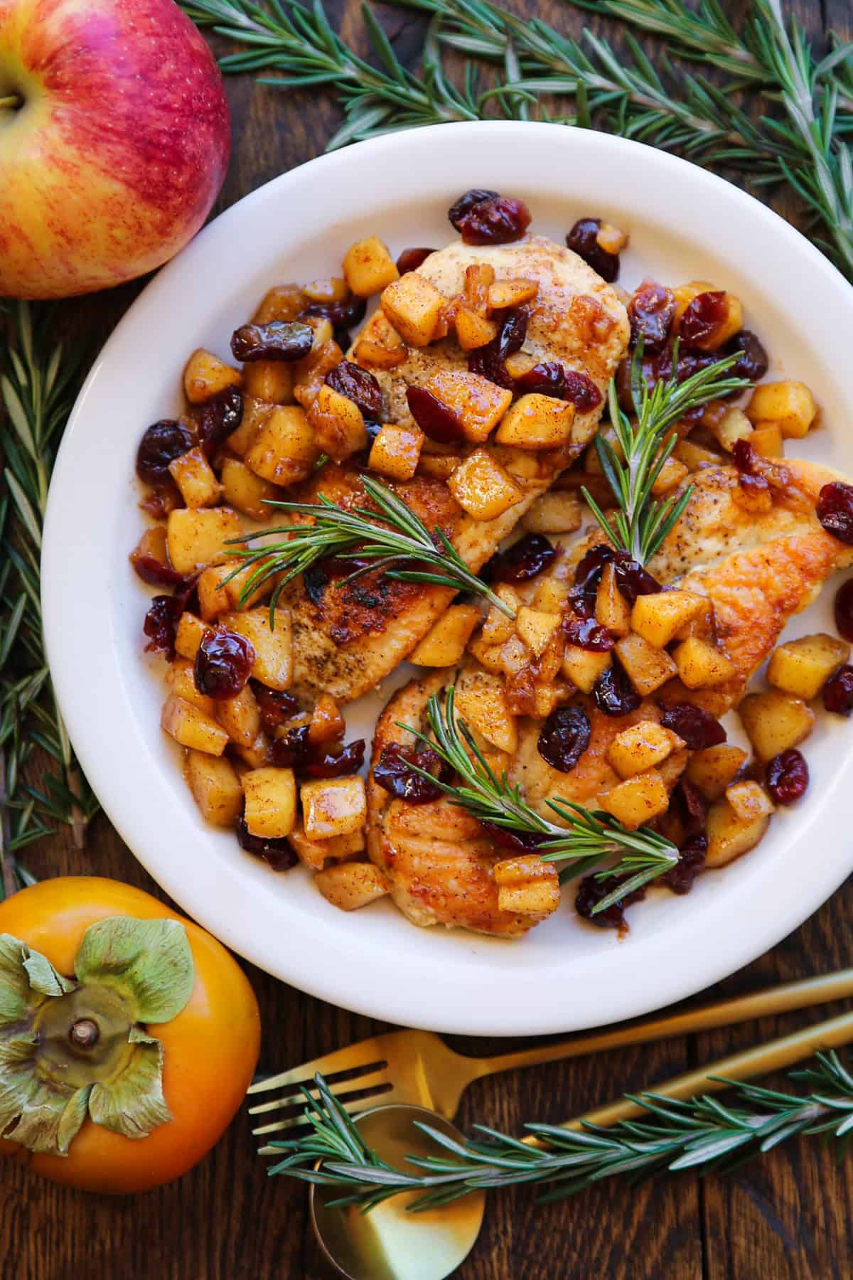 pan-seared chicken breasts with cooked cubed apples, dried cranberries, and cinnamon-honey glaze - on a white plate.