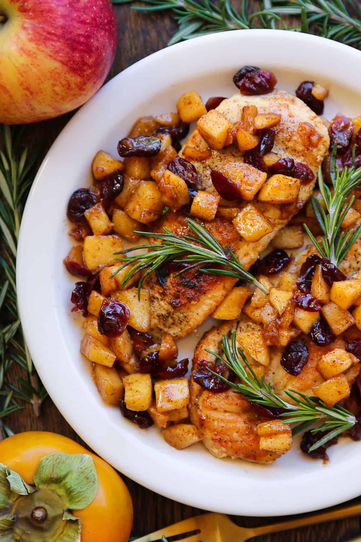 pan-seared chicken breasts with cooked cubed apples, dried cranberries, and cinnamon-honey glaze - on a white plate.