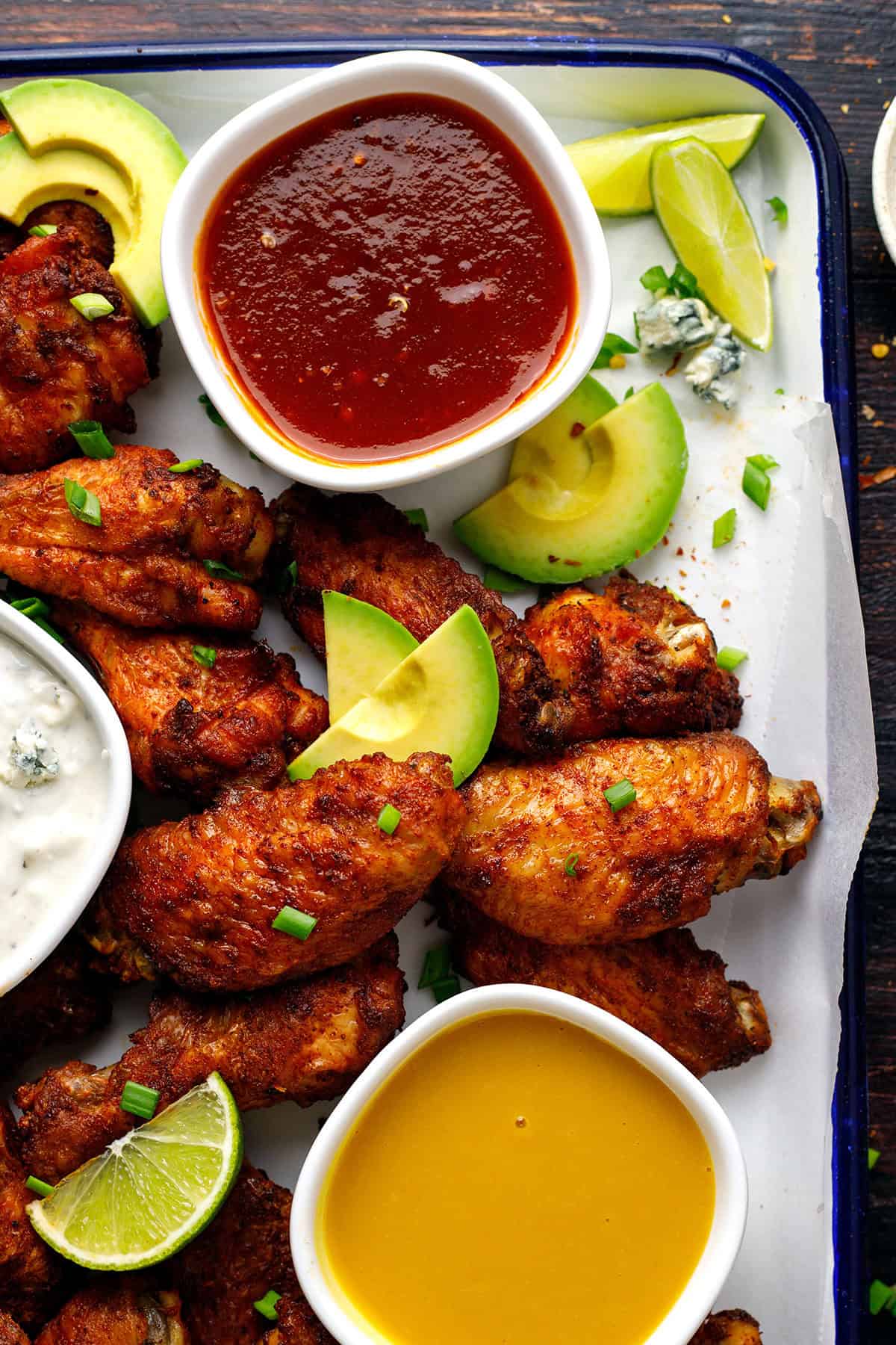 Baked chicken wings with 2 sauces (honey-sriracha and honey-mustard) in small bowls - on a sheet pan.