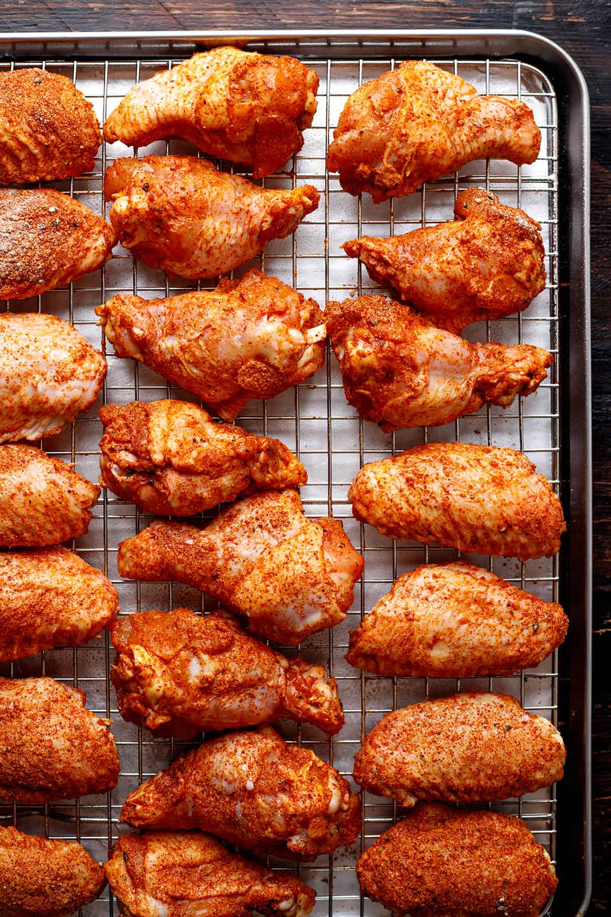 chicken wings with spices on a rack on a sheet pan.