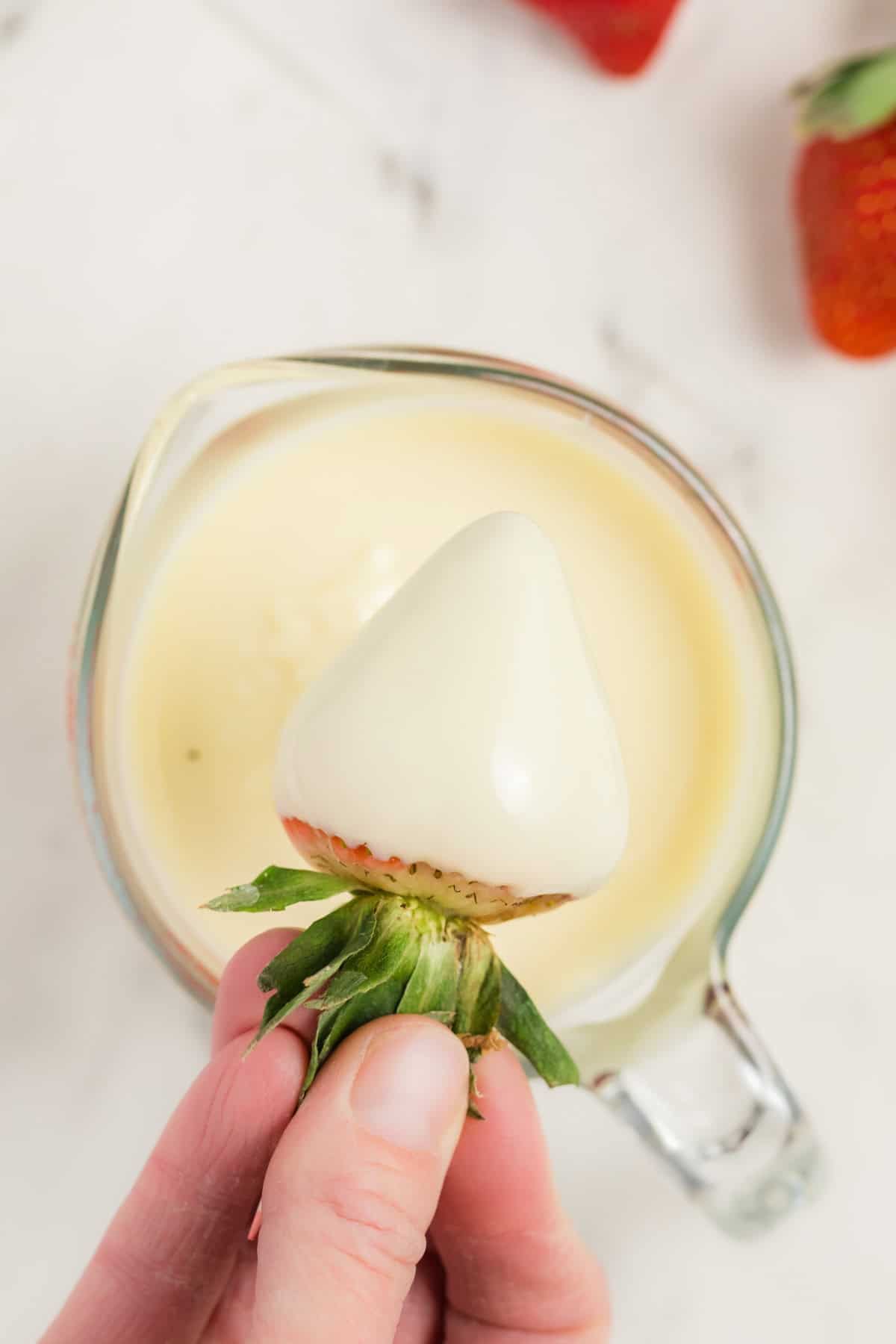 Dipping a strawberry in the melted white chocolate mixture in the bowl.