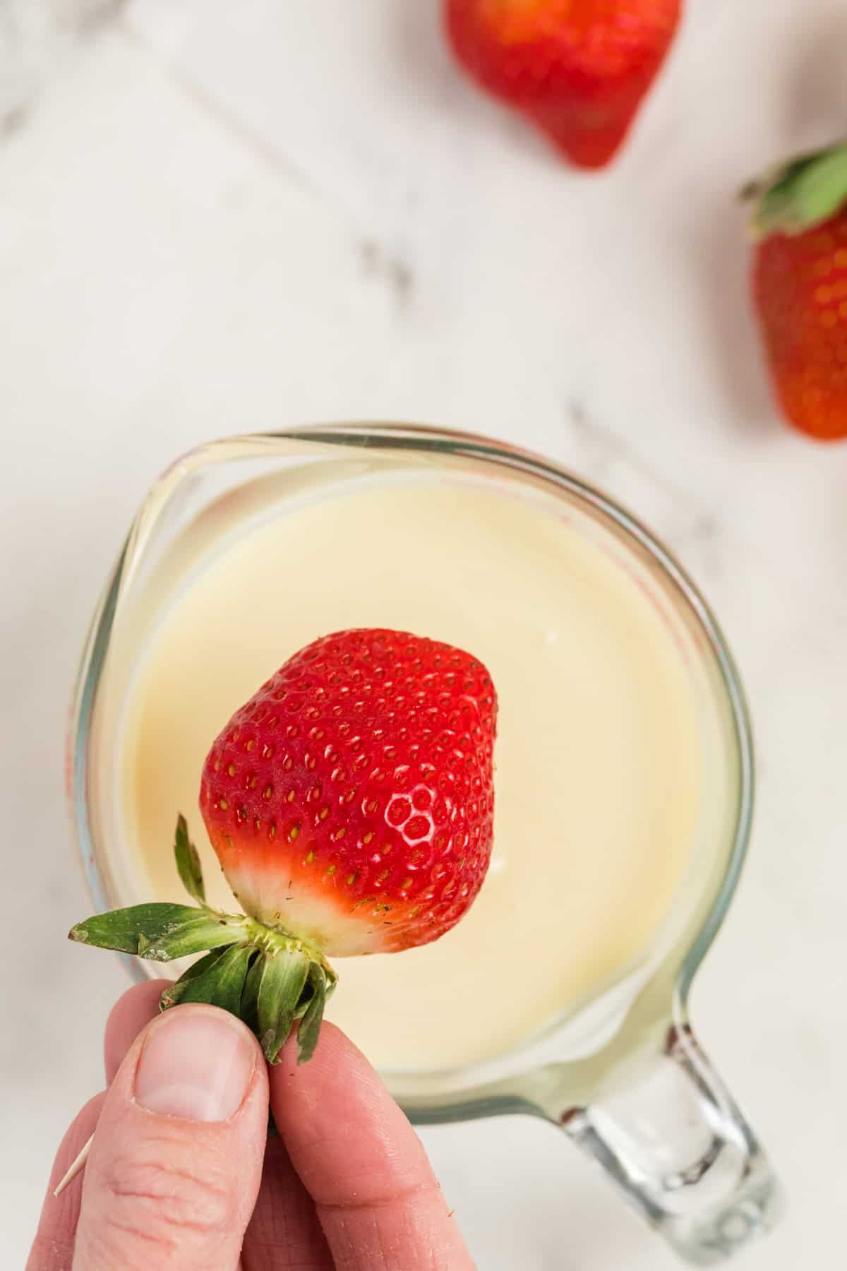 Dipping a strawberry in the melted white chocolate mixture in the bowl.