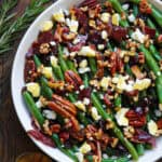 Green bean salad with bacon, pecans, dried cranberries, feta cheese - in a white bowl.