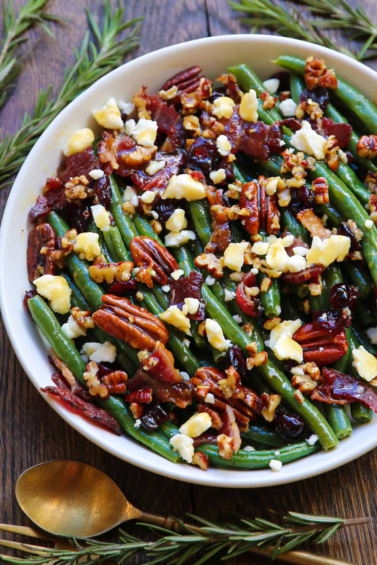 Green bean salad with bacon, pecans, dried cranberries, feta cheese - in a white bowl.