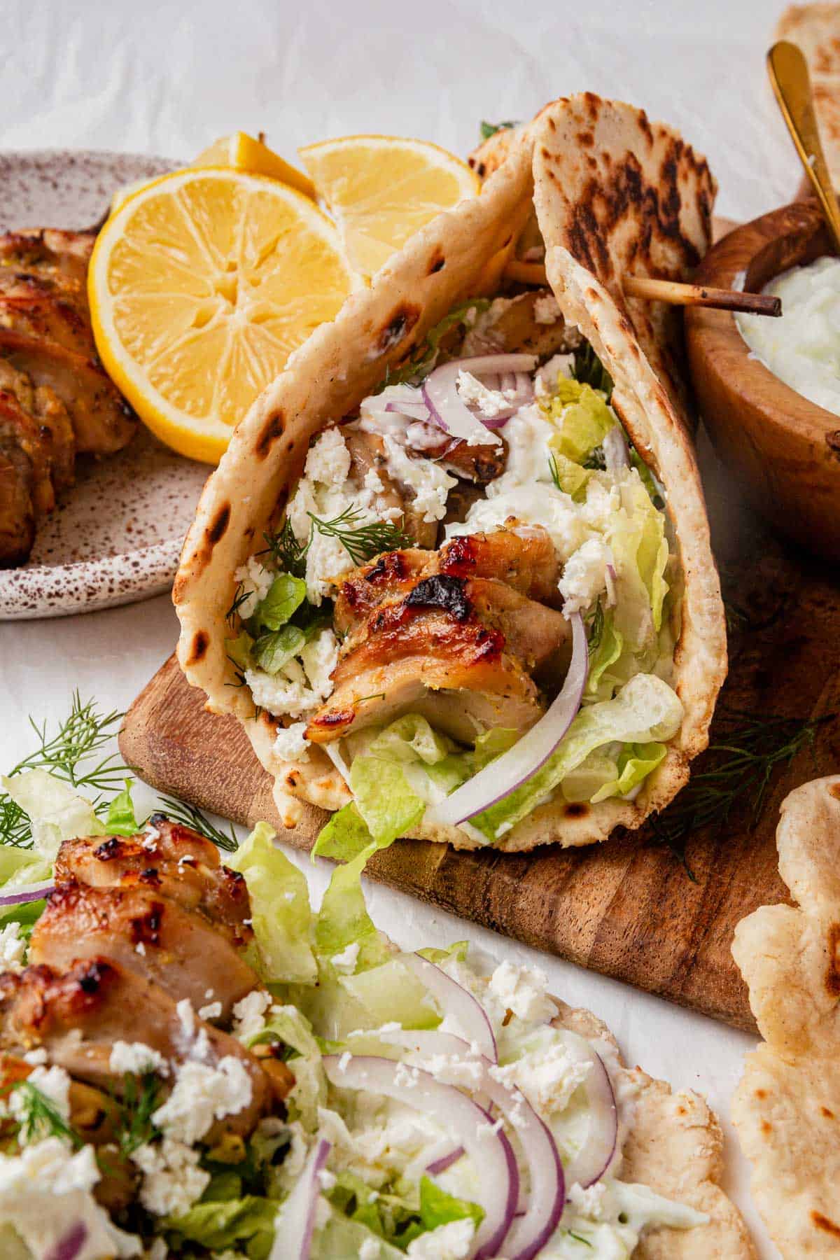 sheet pan chicken gyros assembled in naan with onion and tzatziki.