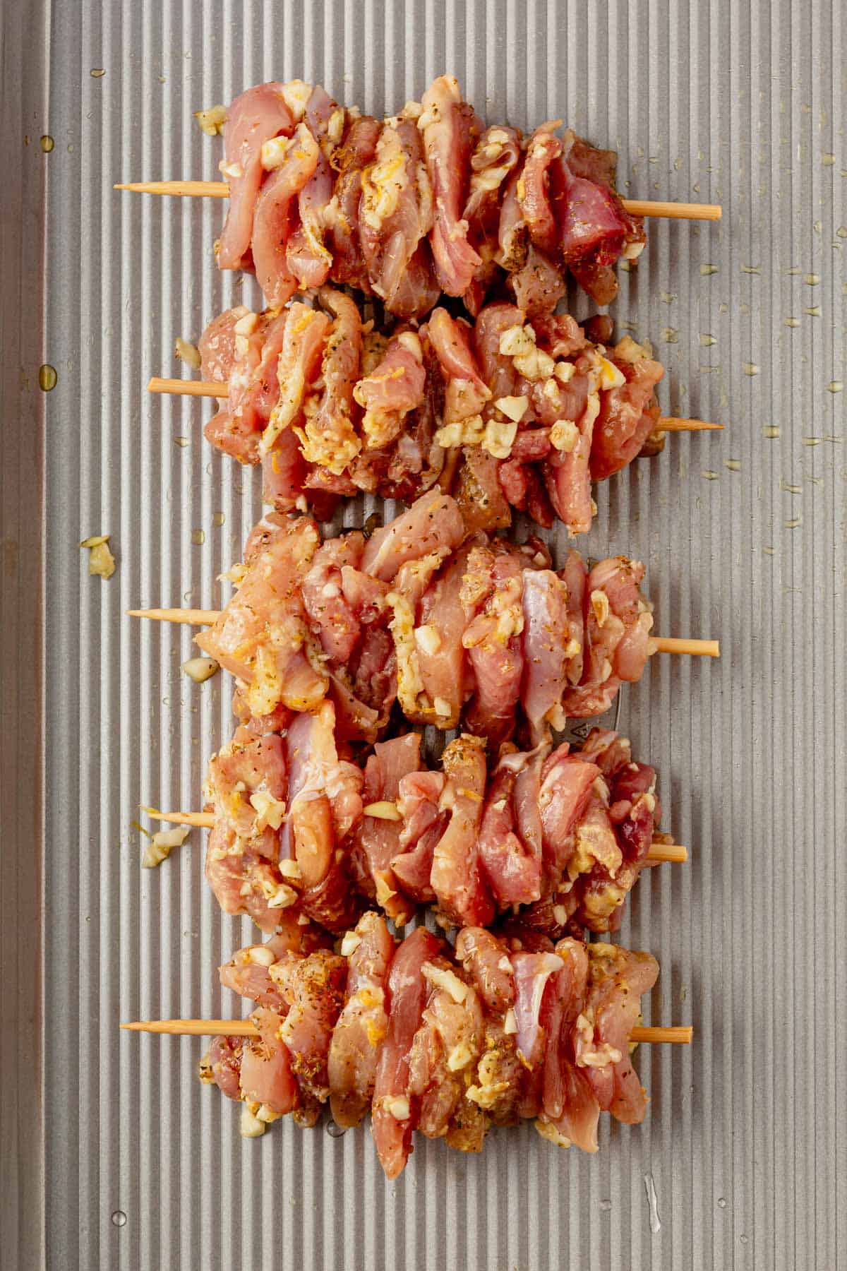 greek chicken threaded onto wooden skewers on a sheet pan.