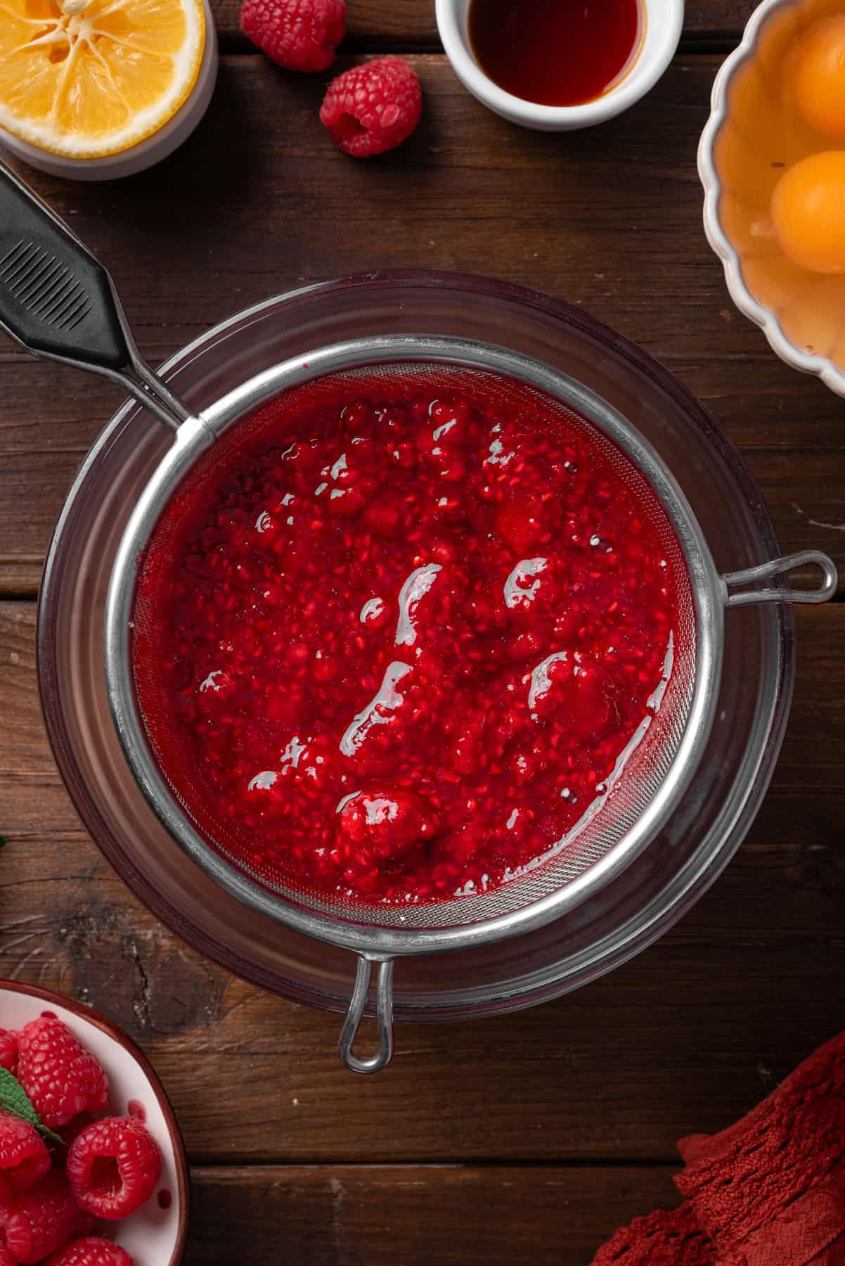 Straining raspberry puree through a fine mesh sieve. 