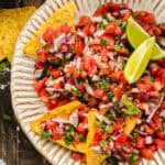Pico De Gallo with tortilla chips and lime slices in a bowl.