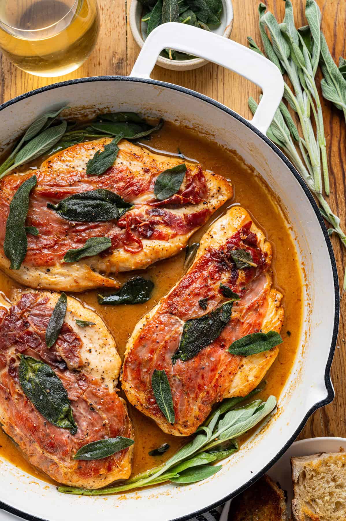 Chicken Saltimbocca (chicken cutlets wrapped in prosciutto and topped with a fresh sage leaf) in a white wine sauce in a skillet.