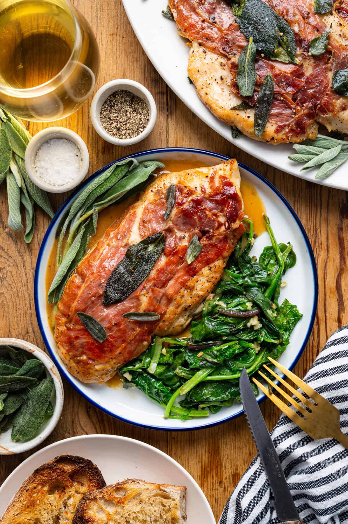 Chicken Saltimbocca (chicken cutlet wrapped in prosciutto and topped with a fresh sage leaf) with wilted spinach on a white plate.