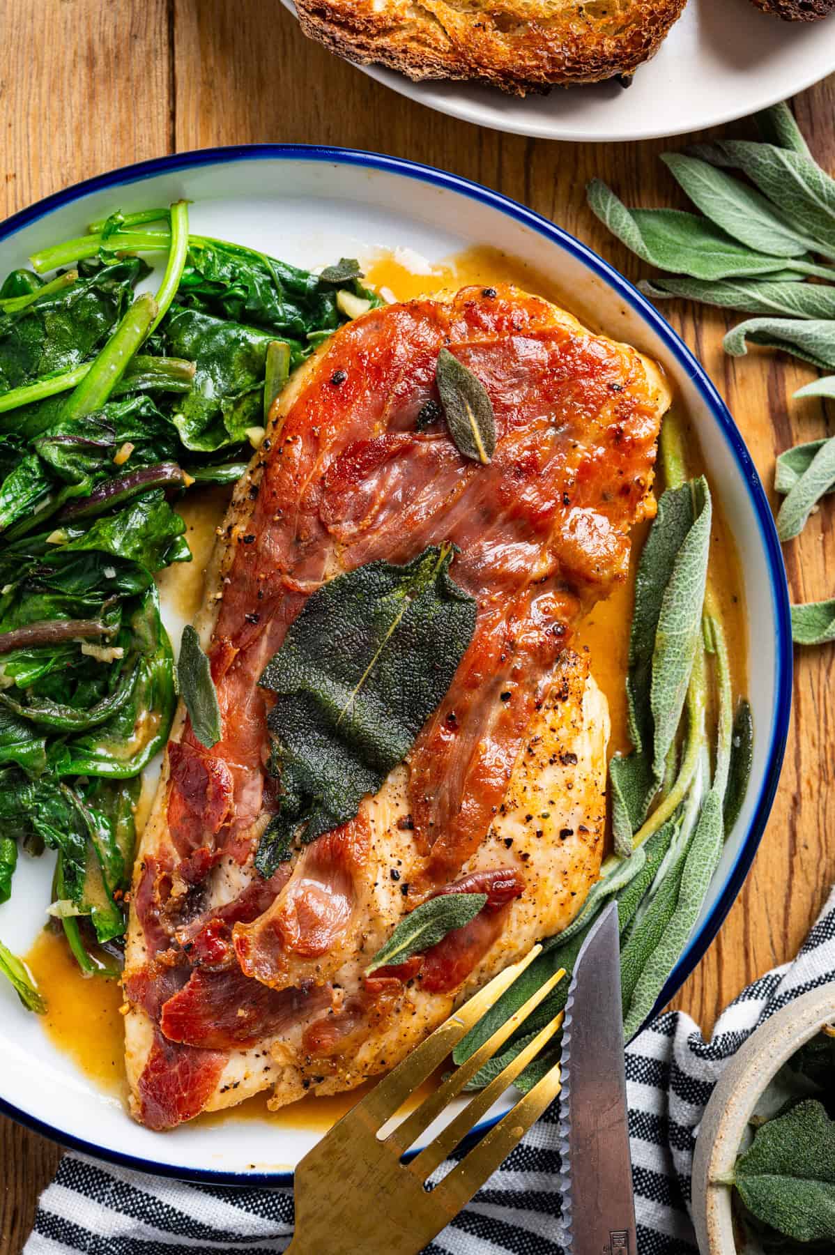 Chicken Saltimbocca (chicken cutlet wrapped in prosciutto and topped with a fresh sage leaf) in a white wine sauce with wilted spinach - on a plate.