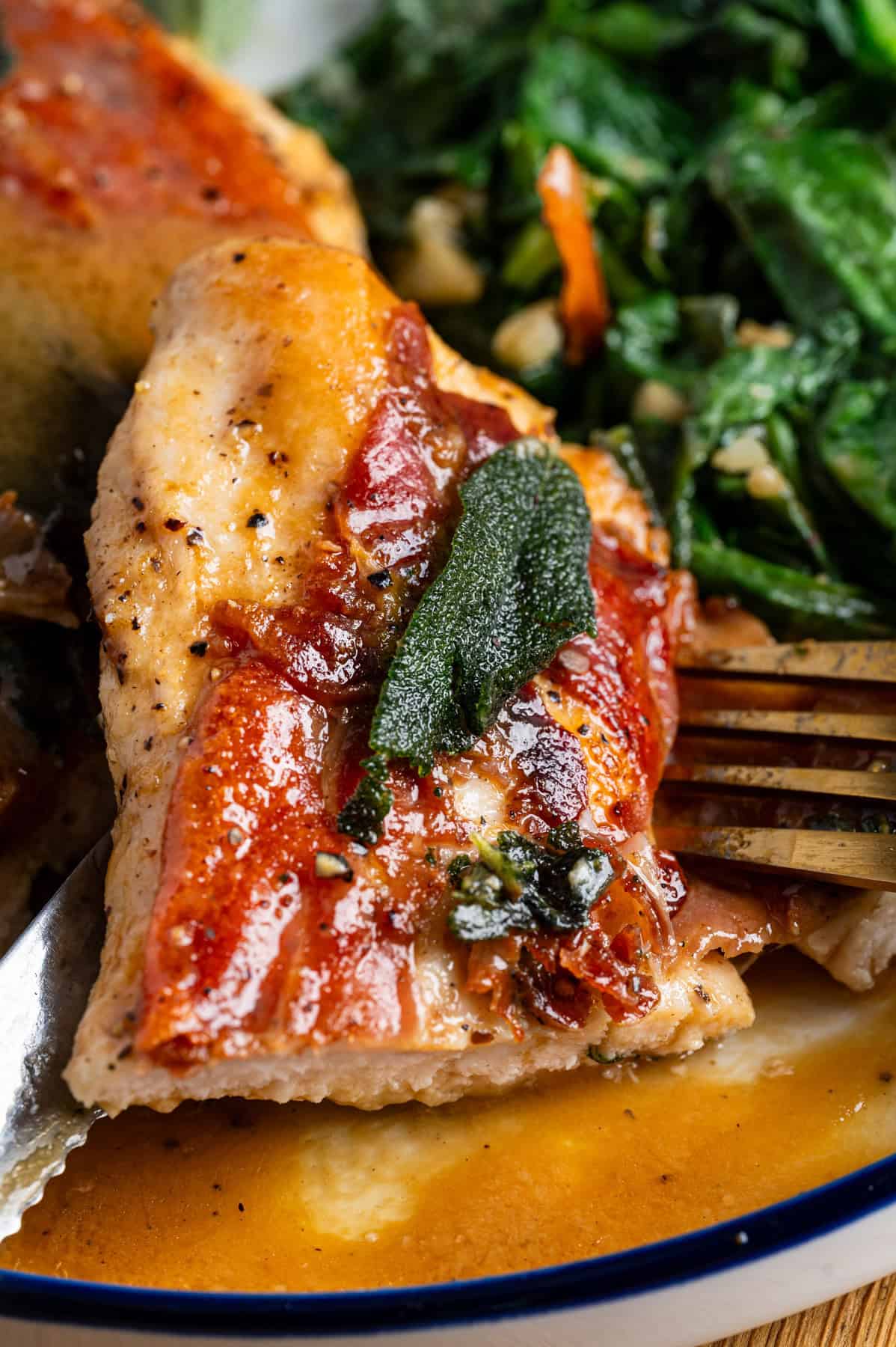 Chicken Saltimbocca (chicken cutlet wrapped in prosciutto and topped with a fresh sage leaf) sliced with a fork on a plate. 