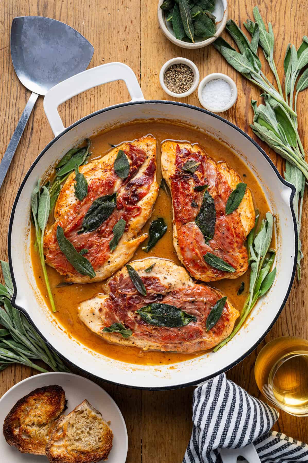 Chicken Saltimbocca (chicken cutlets wrapped in prosciutto and topped with a fresh sage leaf) in a white wine sauce in a skillet.