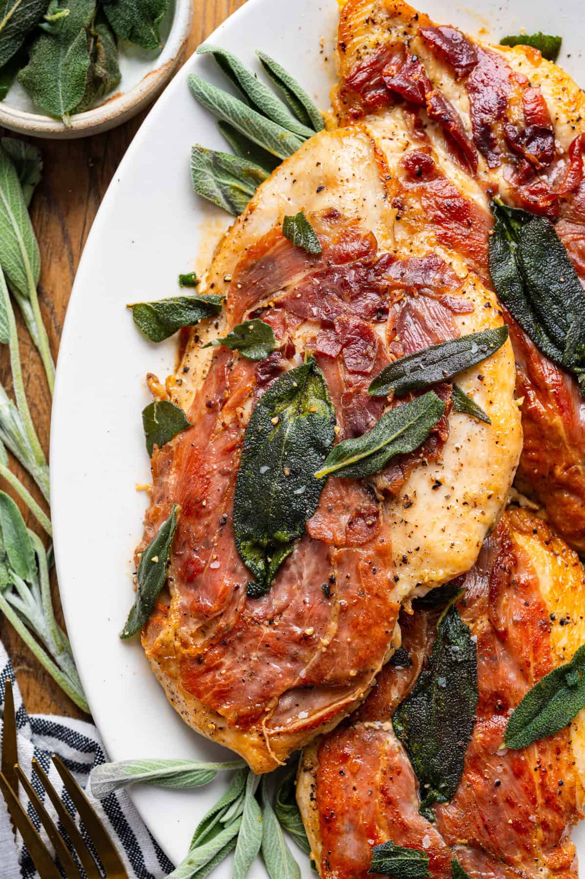 Chicken Saltimbocca (chicken cutlet wrapped in prosciutto and topped with a fresh sage leaf) in a white wine sauce on a plate.