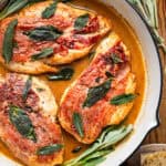 Chicken Saltimbocca (chicken cutlets wrapped in prosciutto and topped with a fresh sage leaf) in a white wine sauce in a skillet.