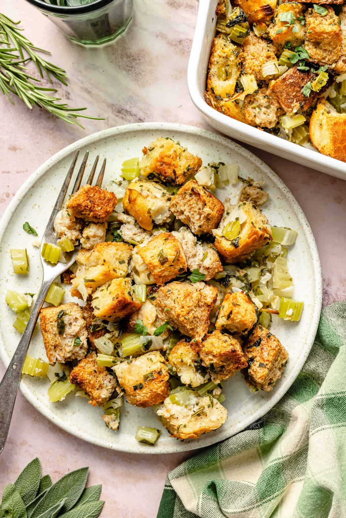 a plate of classic stuffing with butter and herbs on a plate next to the casserole dish.