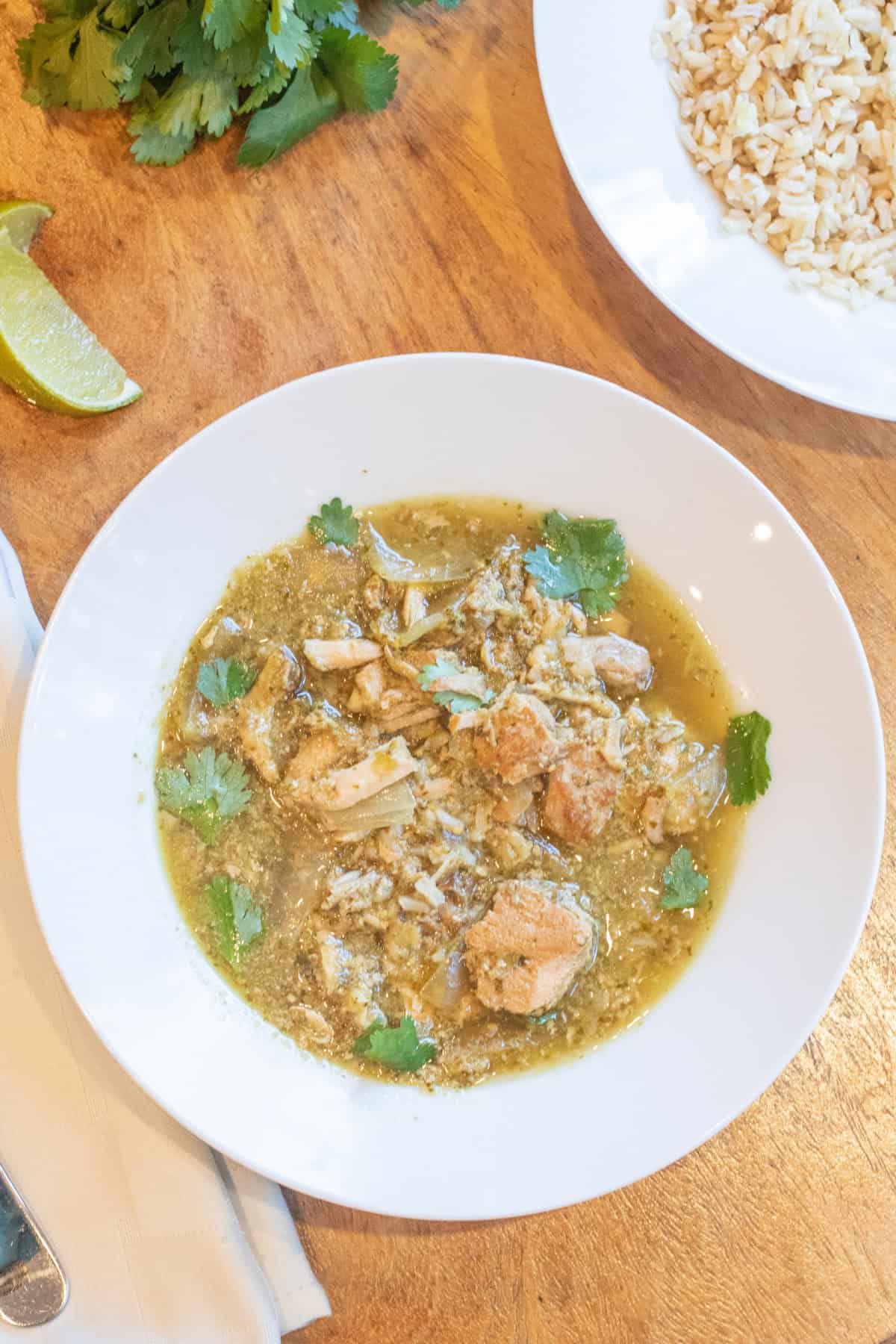 an overhead of a bowl of chili pork verde with a side of rice and some lime wedges.