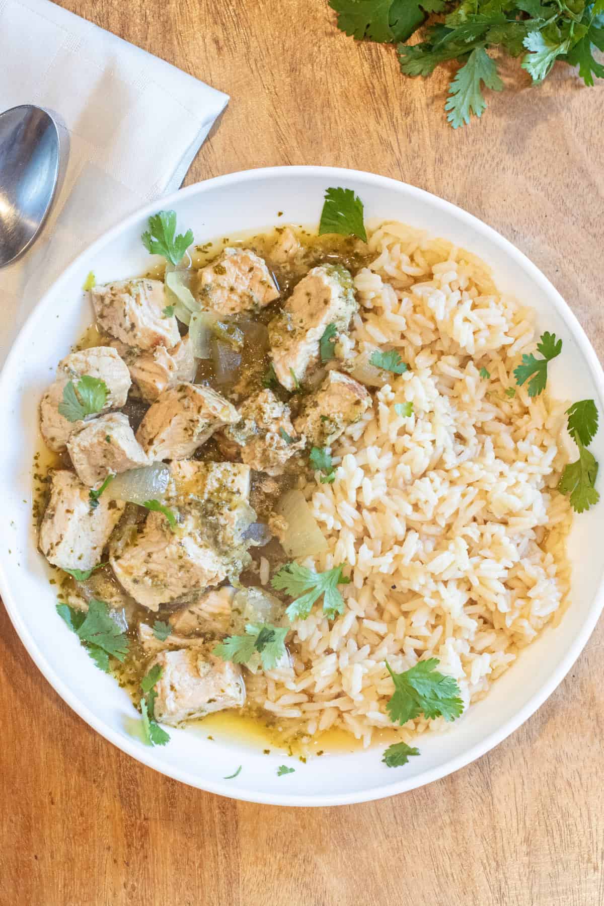 an overhead of a bowl of cubed pork chili verde with rice and fresh cilantro.