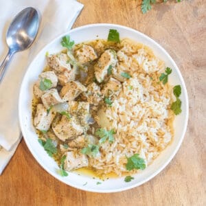 an overhead of a bowl of cubed pork chili verde with rice and fresh cilantro.