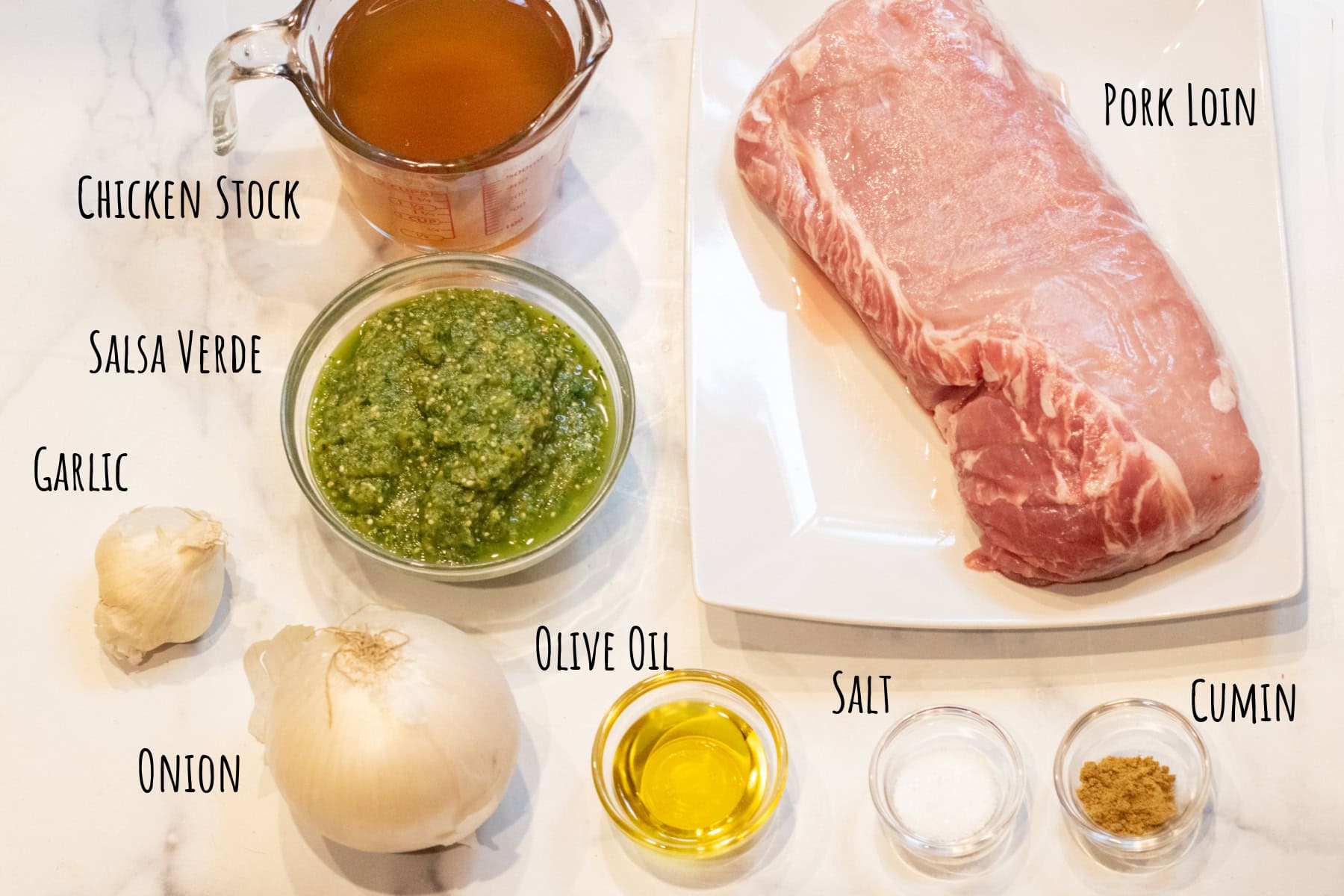 raw pork loin, onion, garlic, olive oil, salt, and cumin, a bowl of salsa verde, and chicken stock all labeled.