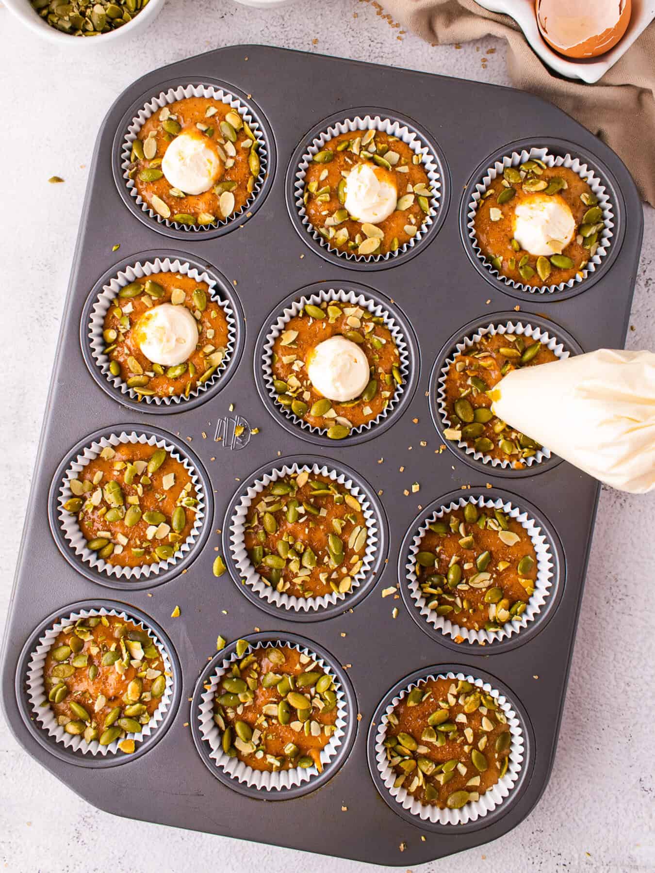 Muffin pan with Pumpkin Cream Cheese Muffins being filled out with cream cheese via piping bag.