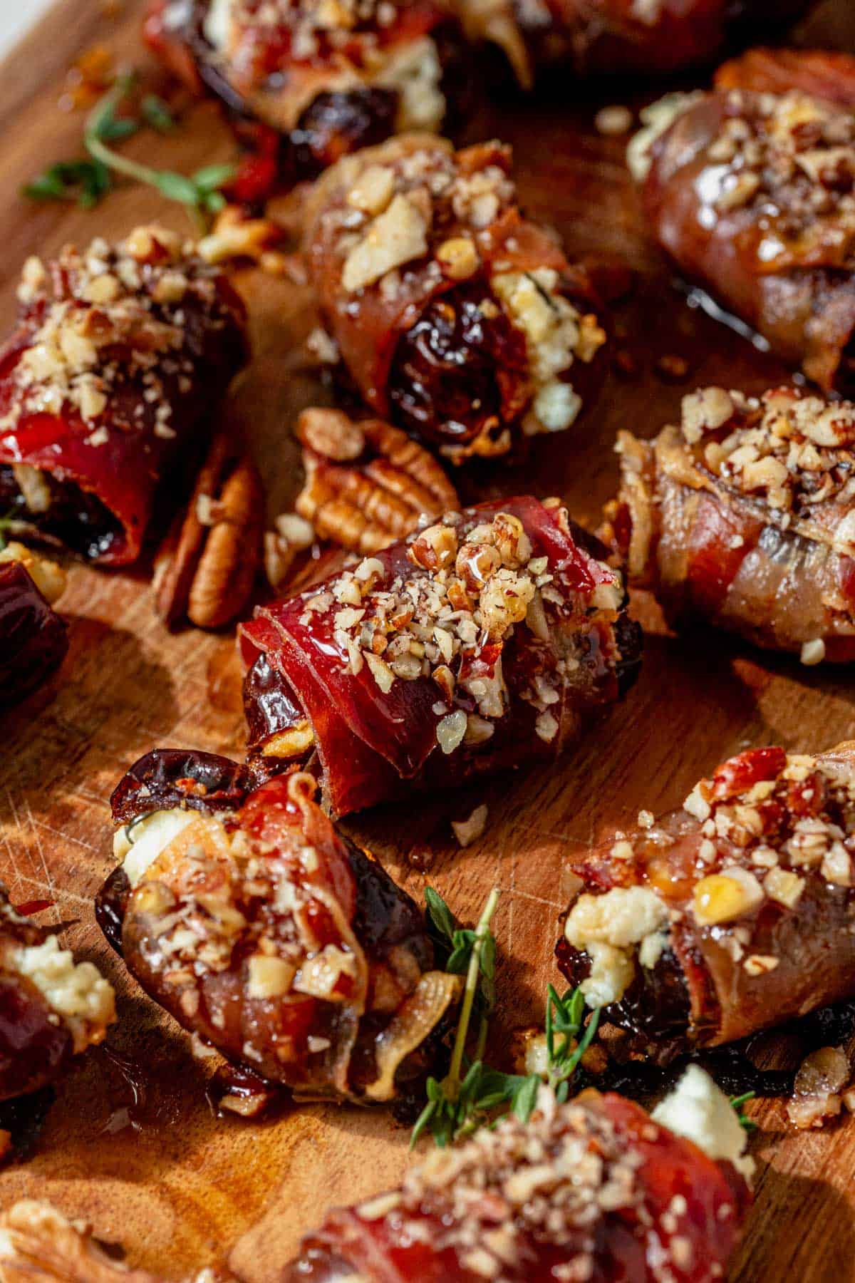 prosciutto wrapped dates drizzled with honey and thyme on a wood serving platter.