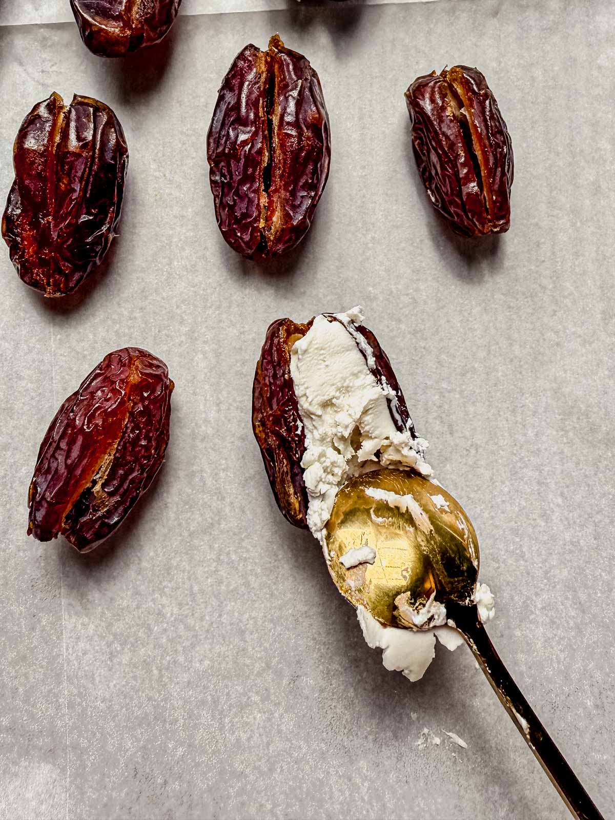 stuffing sliced dates with creamy goat cheese on a baking sheet.