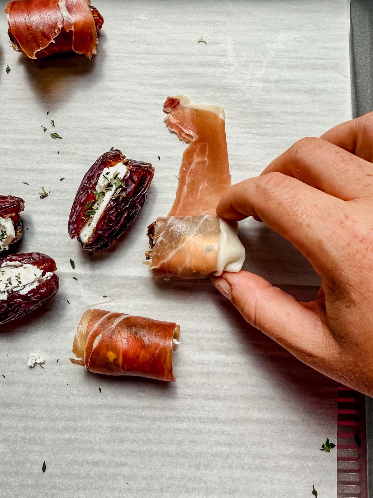 rolling a goat cheese stuffed date in a piece of prosciutto.