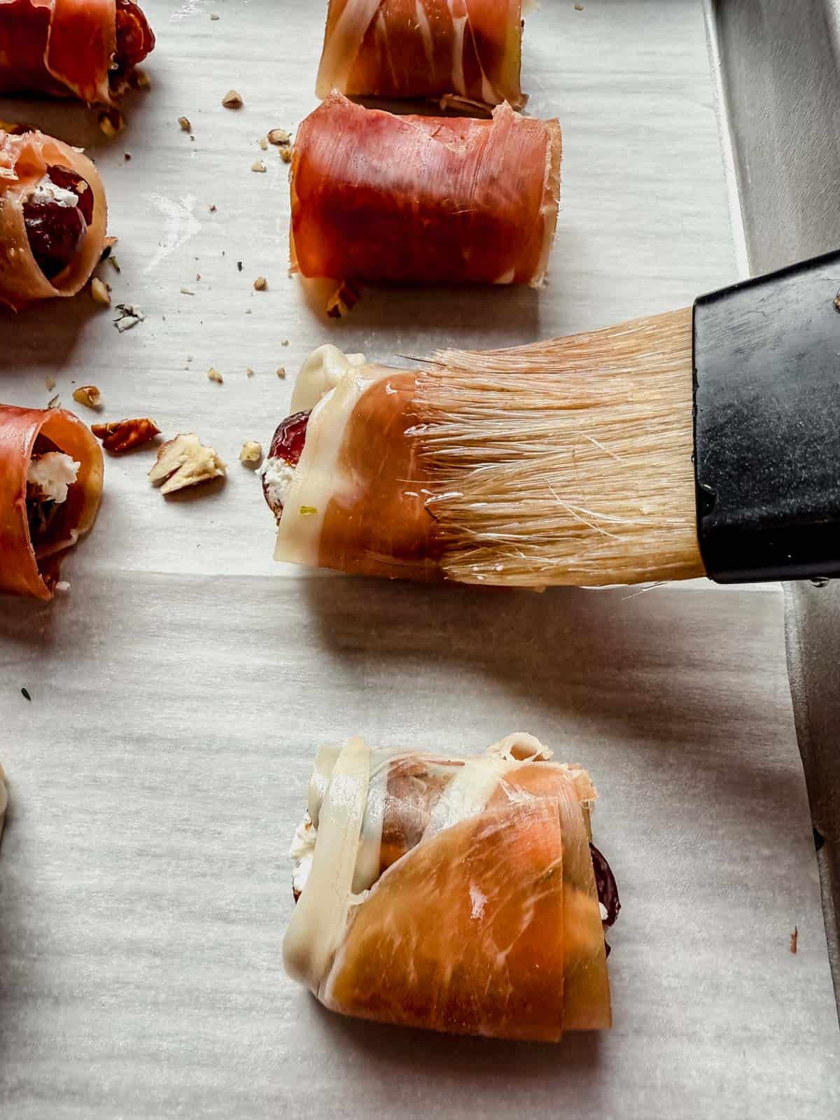 Brushing a prosciutto wrapped date with olive oil before baking.