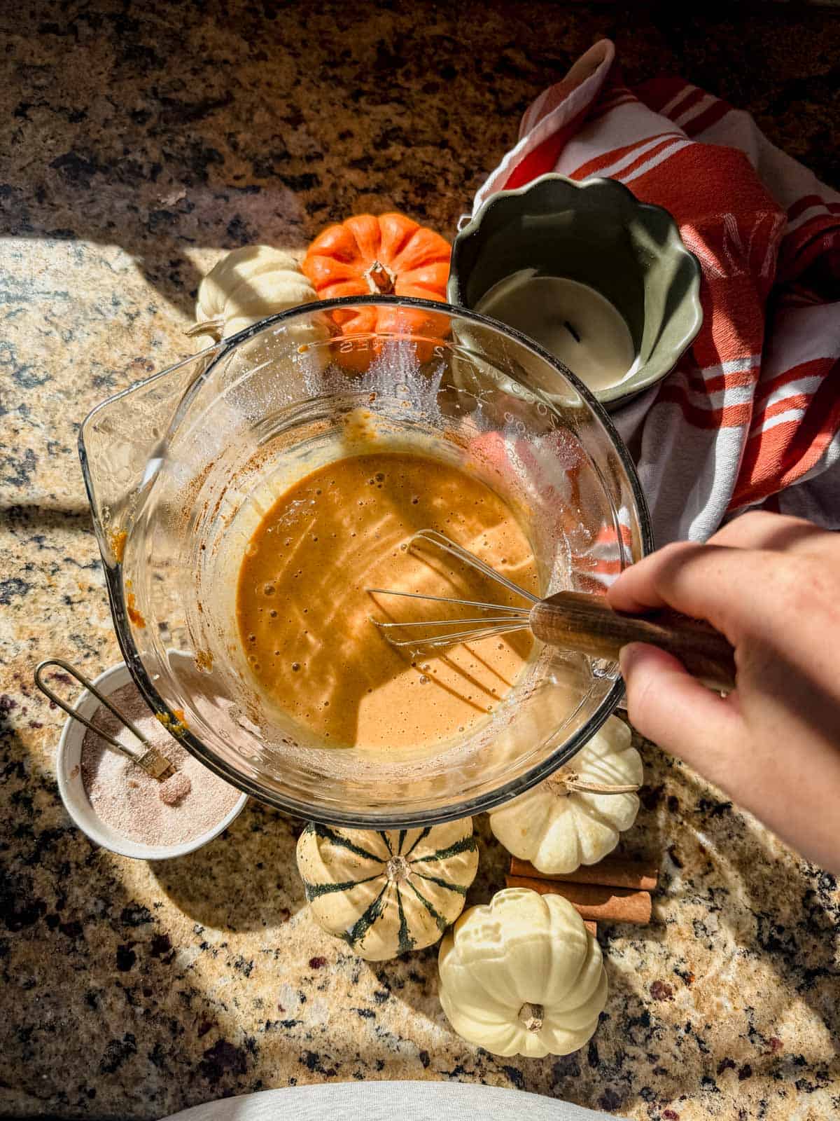 whisking pumpkin pie filling in a glass mixing bowl.