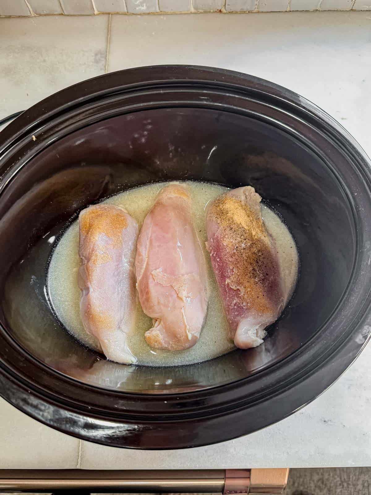 raw chicken breasts, chicken broth, and spices in a slow cooker.
